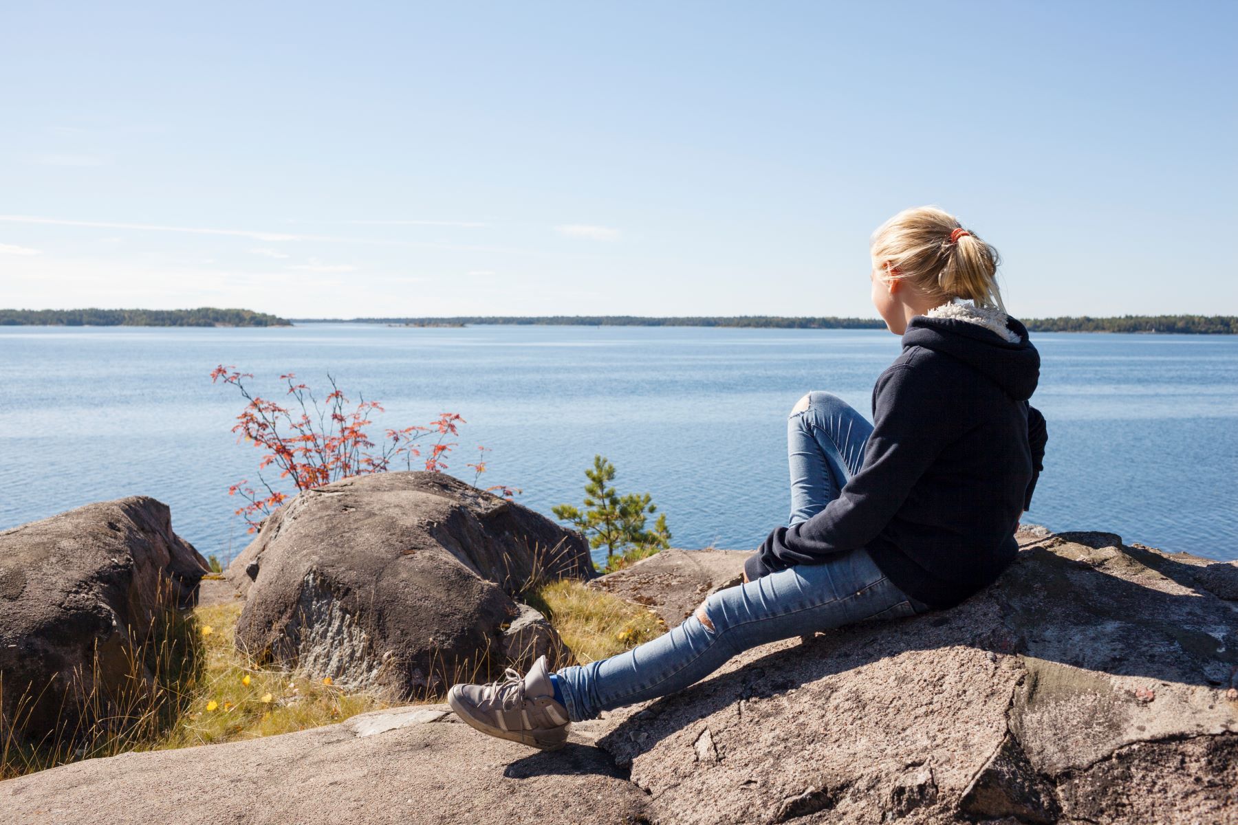 Flicka sitter på en bergsklippa vid havet