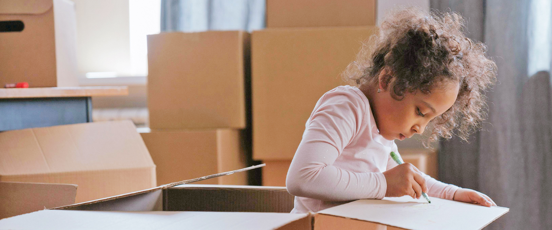 Flicka ritar på ett papper bland flyttkartonger